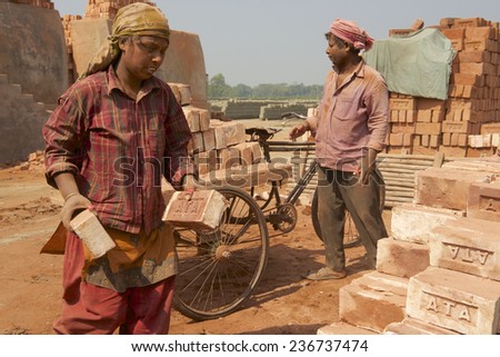 DHAKA, BANGLADESH - FEBRUARY 19, 2014: Two unidentified workers move bricks at a factory on February 19, 2014 in Dhaka, Bangladesh. In Bangladesh women often attend very hard jobs.