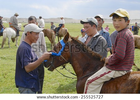 CIRCA HARHORIN, MONGOLIA - AUGUST 26, 2006: Unidentified men attach blue ribbon to the bridle of winner\'s horse. Local horse races in Mongolia are held very often.