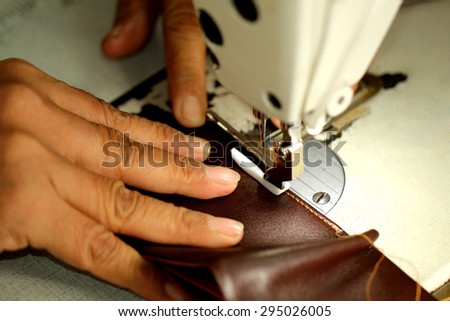 Tailor working on a sewing machine at textile factory / Old women\'s hands with sewing machine at textile factory