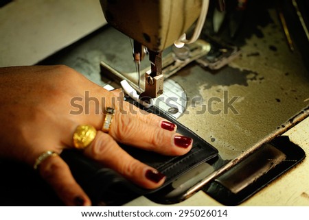 Tailor working on a sewing machine at textile factory / Old women's hands with sewing machine at textile factory
