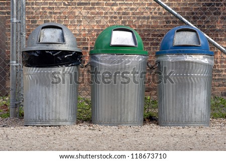 Three trash cans for recycling in front of brick wall
