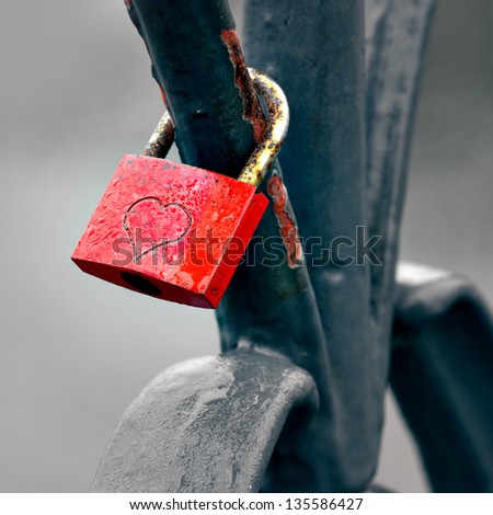 Red padlock with heart locked to bridge railing on rainy gloomy day