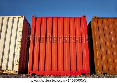 Low angle view of three shipping containers in different colors on blue sky