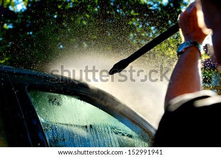 man washing car in sunshine with high pressure washer