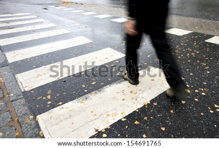 Man in black crossing street on wet autumn day