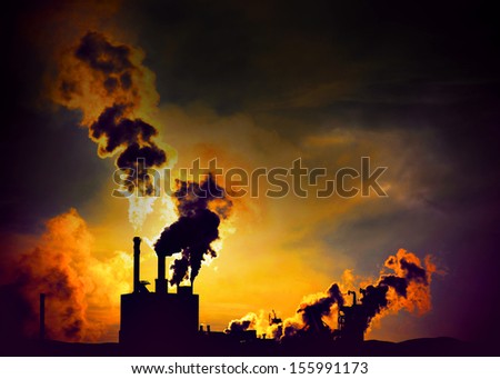 Silhouette of factory with chimneys and heavy orange smoke at night