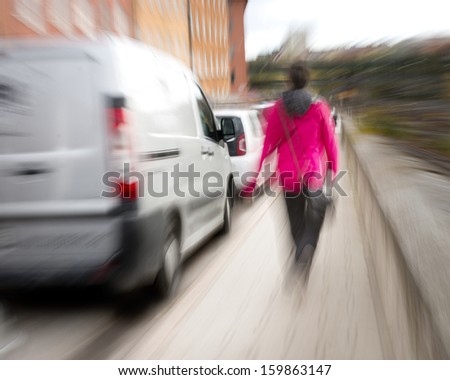 Woman in blurred motion dressed in red walking along sidewalk in busy street
