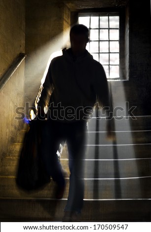 Silhouette of back lit man with bag walking in staircase with sunbeams coming through window