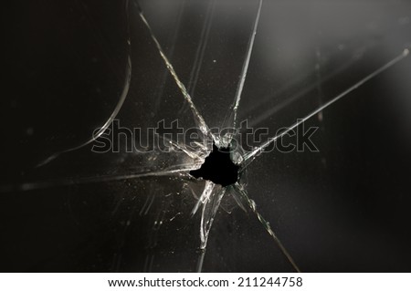 close up of smashed glass window with small black hole