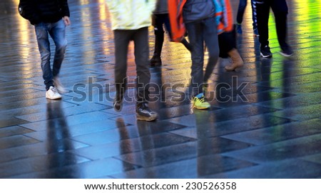 Feet of people on wet pavement with reflection of colorful lights