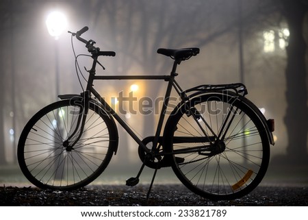 Silhouette of parked bicycle in park at foggy night in autumn