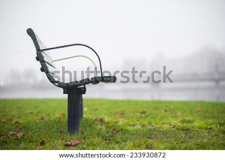 Empty wet park bench on foggy autumn morning