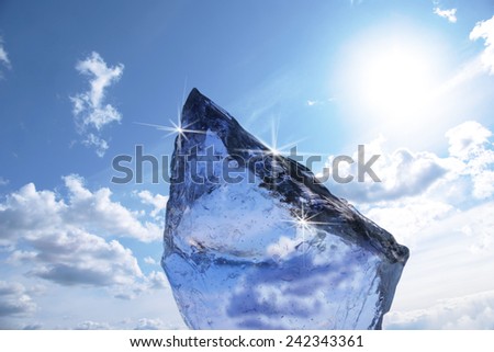 Block of ice with reflection of sun on blue sky