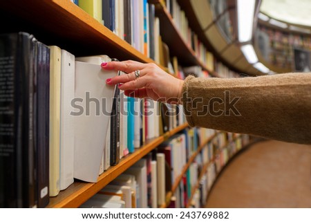 Hand of woman selecting a book from book shelf