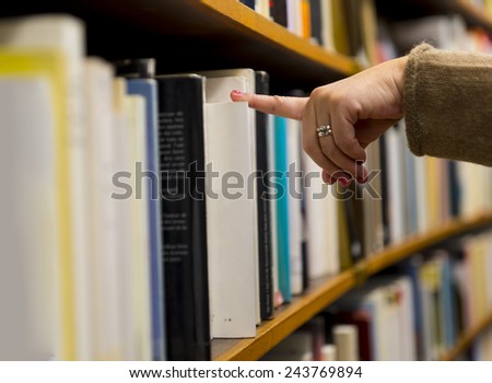 Hand and finger of woman selecting a book from book shelf