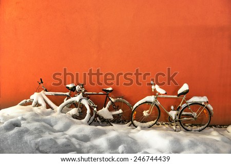 Bikes in winter by orange concrete wall covered in snow