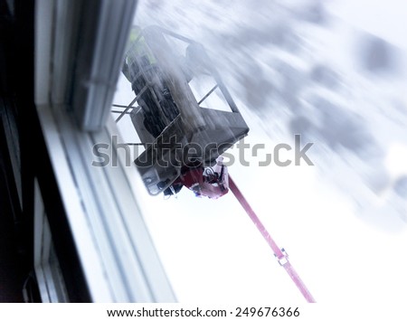 Man using hydraulic construction cradle to clear snow on roof, seen through window