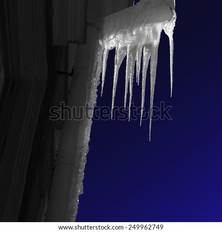 Icicles on pipe on facade of building at night, with dark blue sky