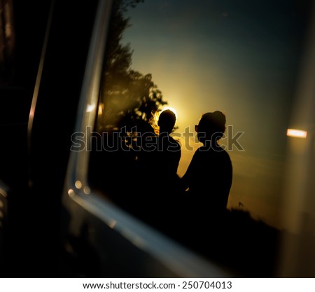 Silhouette of couple reflected in car window at sunset
