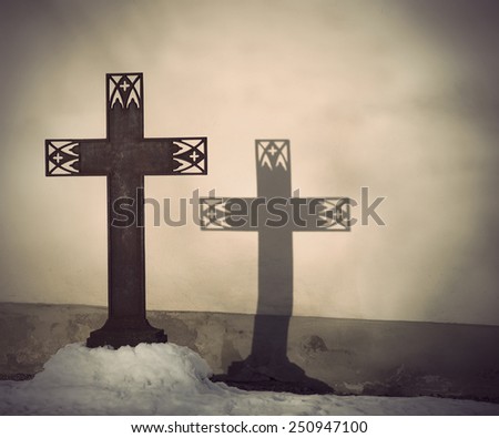 Rusty metal Christian cross with shadow on church wall. Focus on shadow.
