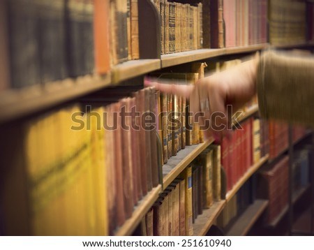 Library or book store with rows of old antique books, and a hand of a woman reaching for a book