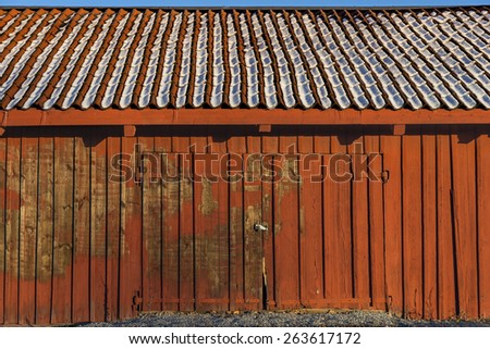 Red shed of weathered wood with snow on tiled roof and door with padlock