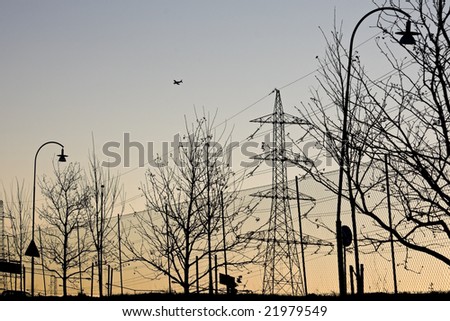 Silhouette of an electricity pylon, trees, lamp posts and road signs along a a main road.