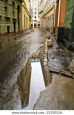 The rain just stopped, and the buildings along the narrow Budapest street are reflected in a puddle.