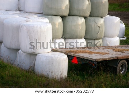 Stack of hay bales wrapped in plastic and an empty trailer