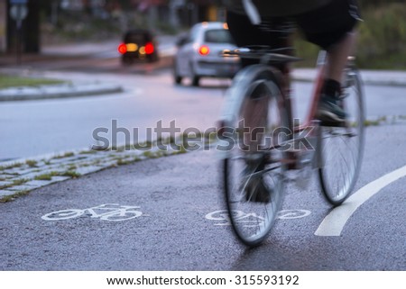 Cyclist in blurred motion on cycling path by busy street at night