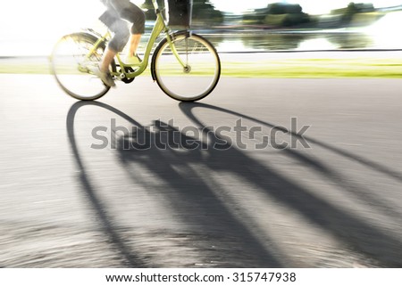 Person cycling along river in bright sunshine, casting long shadow on cycling path