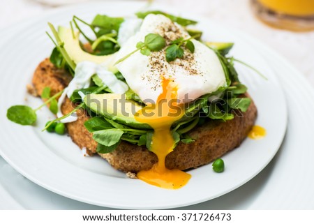 Healthy Breakfast with Wholemeal Bread Toast and Poached Egg with Green Salad, Avocado and Peas. Orange Juice and Orange Slices on the Background.