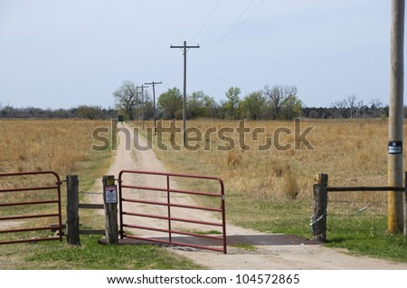 Open gate and lonely little road lead to a family farm on the horizon.  There is a no-trespassing sign on the post to the right.