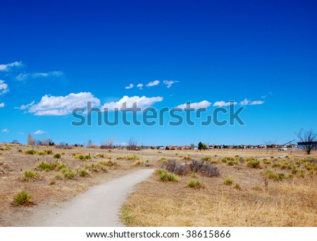 Path leads through rural prairie scenery, with a line of distant new homes on the horizon