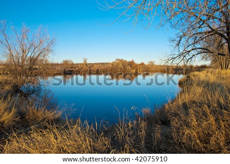Clear blue lake with reflections in the Colorado prairie with tiny homes on the horizon
