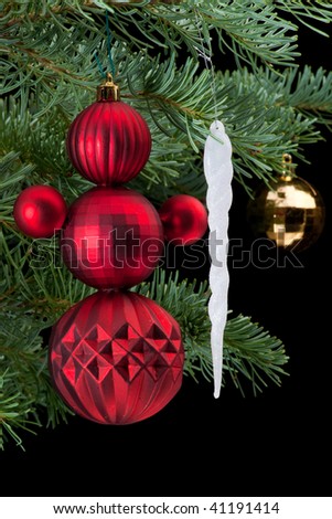 Snowman made from red baubles holding white icicle christmas ornament on fir tree branch. Black background. Vertical composition.