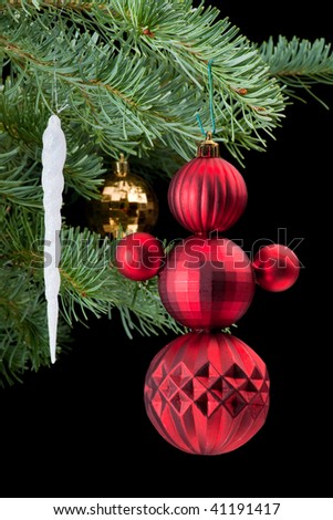 Icicle and snowman made from red baubles christmas ornaments on fir tree branch. Black background. Vertical composition.
