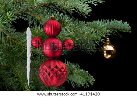 Snowman made from red baubles holding white icicle christmas ornament on fir tree branch. Black background. Horizontal composition.