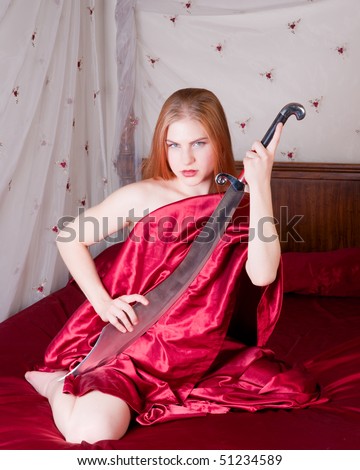 Gorgeous strawberry blond draped in red satin sheets holding a scimitar sitting on canopied bed