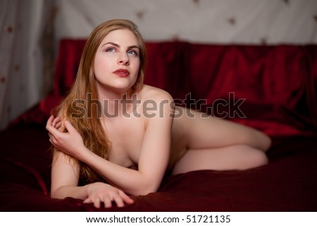 Beautiful strawberry blond woman on red satin sheets. Shallow depth of field.