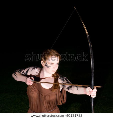 Beautiful redhead girl in celtic tribal makeup drawing a bow
