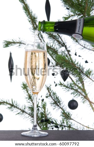 Sparkling wine poured into fluted champagne glass with christmas tree in background
