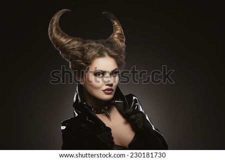 Girl with devil horns in a black pvc and leather shiny suit and spiky collar