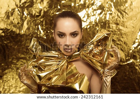 Beautiful young girl in shiny golden metallic dress and long gloves posing on gold background