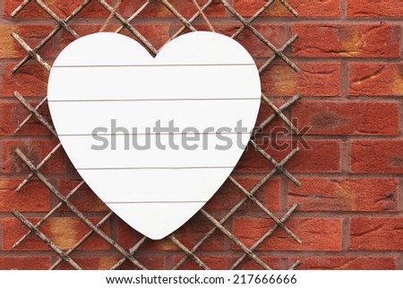 White Shabby Chic wooden heart hanging on a trellis set against a red brick wall. Copy Space for your text on the heart.