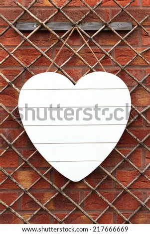 White Shabby Chic wooden heart hanging on a trellis set against a red brick wall. Copy Space for your text on the heart.