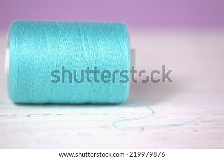 Haberdashery pink thread on white rustic wooden and lilac background, macro, close up,