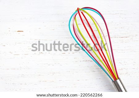 colorful whisk on white distressed wood chopping board. Kitchen/baking background.