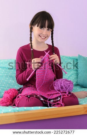 Young girl knitting a pink scarf.