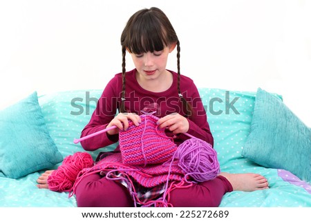 Cute little girl knitting a scarf with vibrant colored wool in a domestic setting.